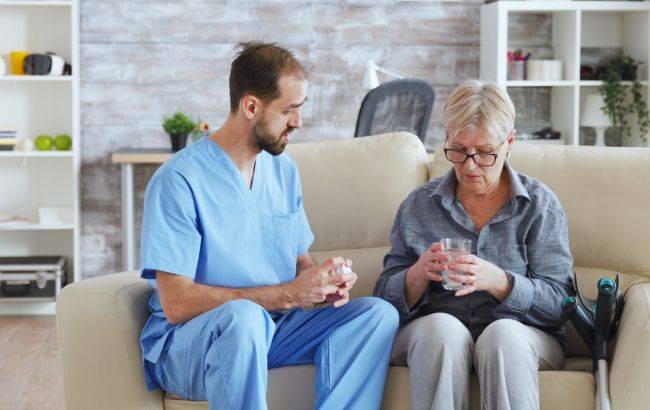 male_nurse_sitting_couch_with_senior_woman_giving_her_medical_treatment_nursing_home_650x410